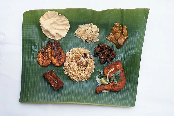 Indian food served on a coconut leaf, including, biryani seasoned rice cooked with vegetables, nuts and saffron with brinjal, cabbage, mutton masala, chicken masala, poppadam, prawn masala and chicken tikka