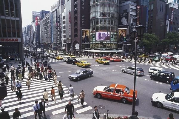 Japan, Tokyo, Centre, pedestrians and cars at Ginza-Yon-chome crossing, dominated by rounded glass front of San ai Building, high angle view