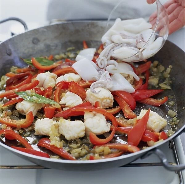 Making paella, adding bowl of squid to pan of onion, garlic, red pepper and monkfish