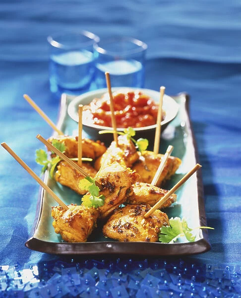 Saffron chicken skewers served with red sauce on rectangular tray