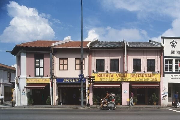 Singapore, Little India, row of restaurants and shops, painted pink and white, shuttered windows, awning over shop fronts, red traffic light, cyclist on rickshaw passing, pedestrian walking