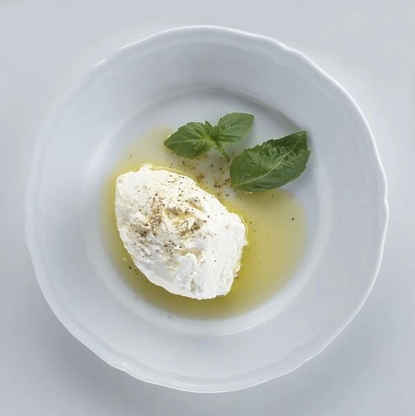 Slice of ricotta with olive oil, black pepper and basil leaves on a plate, view from above
