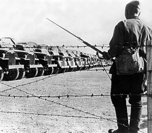 A soldier standing guard over a long line of american trucks at a lend-lease depot in iran, the trucks arrived and were assembled in the persian port and are now awaiting shipment to the soviet union