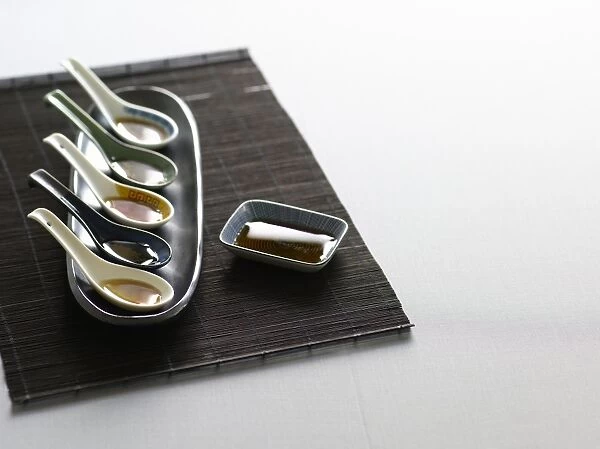 Spoons containing various types of Vietnamese and Thai fish sauce, on bamboo place mat