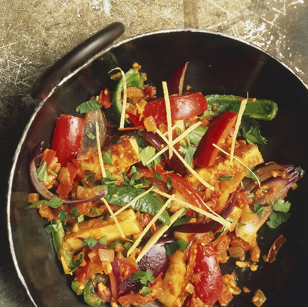 Stir fry including paneer cheese, peppers, onion, herbs, in large pan, overhead view