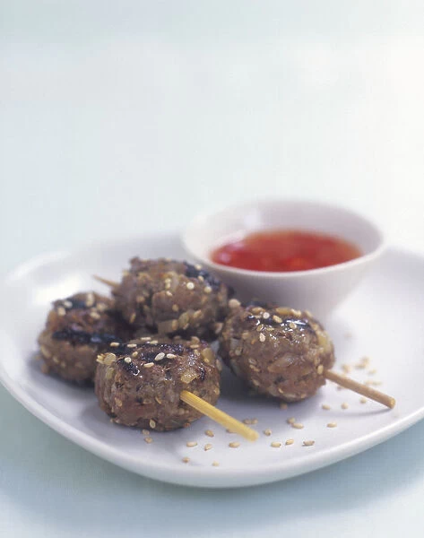 Vietnamese mini kebabs (Cha bo) on wooden skewers served with savoury sauce on white plate, close-up