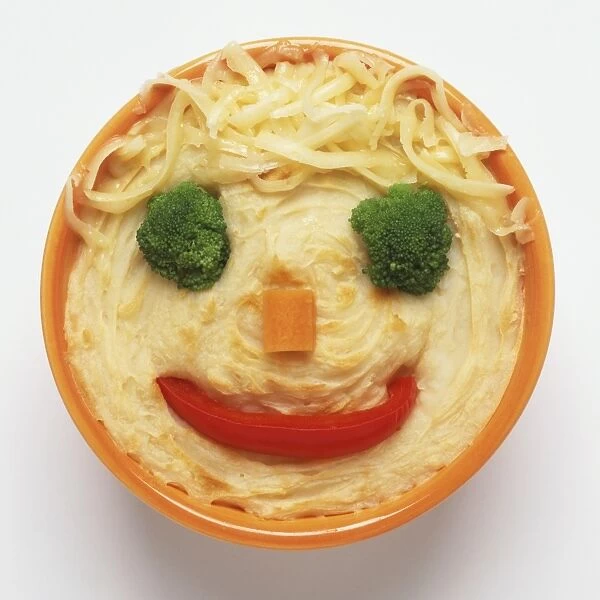 Above view of a shepherds pie with a smiley face on it made from vegetables