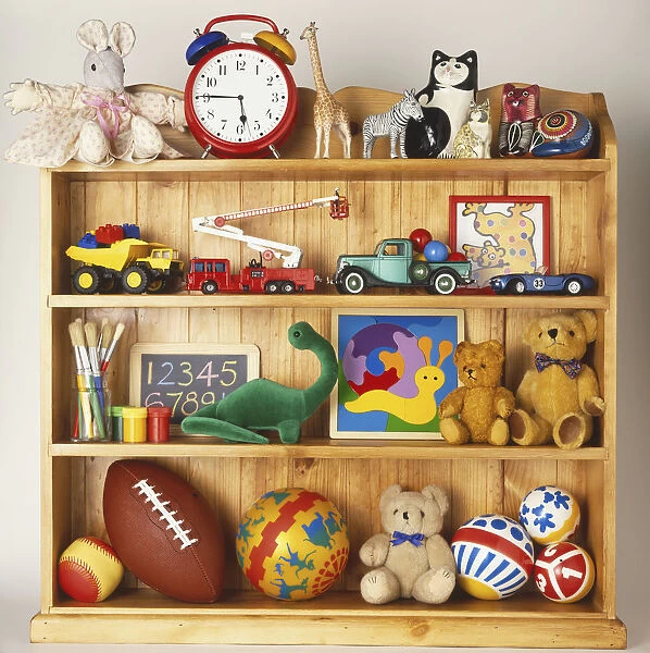 Wooden bookcase stacked with toys including rubber balls, cuddly animals and plastic cars and trucks