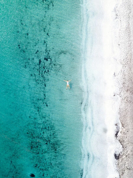 Woman takes a bath and floats in a turquoise sea. Stintino, Sardinia, Italy. Aerial view