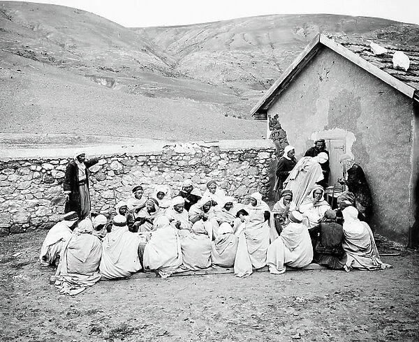 Algeria, Ain zeft: Algerians squatting on the ground eat in a mountainous landscape, 1906