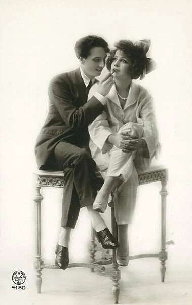 Androgynous man in suit applying lipstick to lips of girl in pyjamas (b  /  w photo)