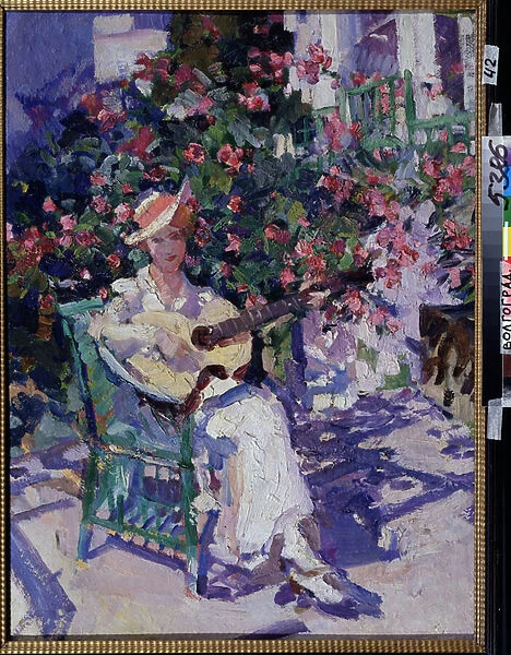 En Crimee (In the Crimea). Une jeune femme en robe claire et legere assise sur une chaise de jardin, devant un bosquet fleuri, joue de la guitare, en plein ete dans la region balneaire du golfe de Crimee