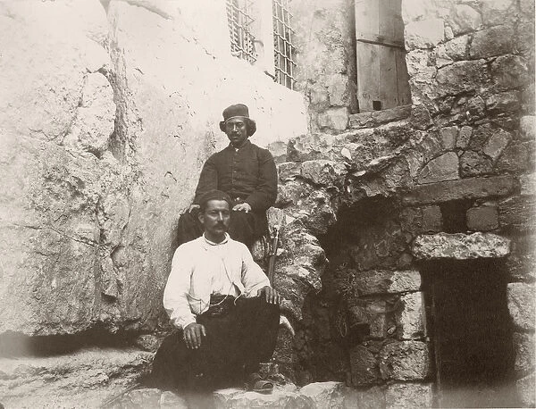 Two men sitting next to the lintel of Barclays Gate in the Western Wall of Temple