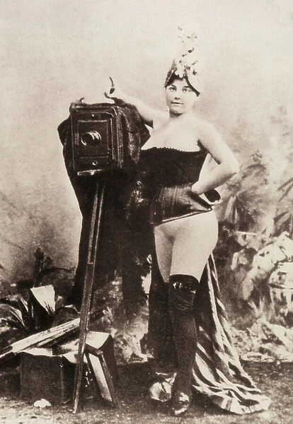 Portrait of a partially nude woman leaning on an antique camera