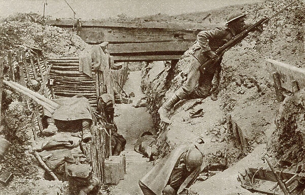 Soldier keeping watch whilst his comrades sleep in a trench during World War One. From The Story of 25 Eventful Years in Pictures published 1935