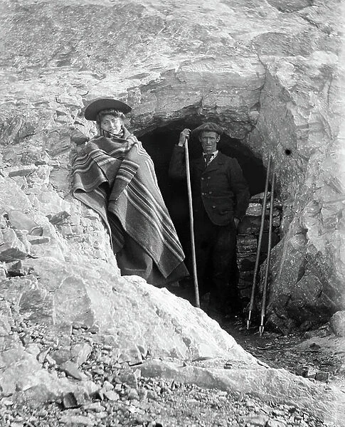 Switzerland: A climber and her guide resting at the entrance of a cave, 1900