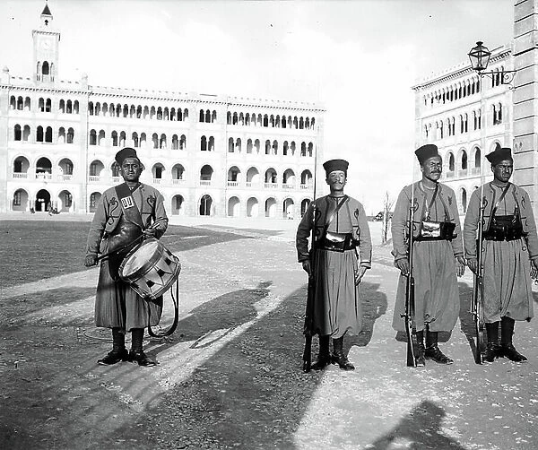 Tunisia, Bizerte: Group of four shooters, one with a drum and the other three with rifles stand guard at the entrance of the new barracks, 1905