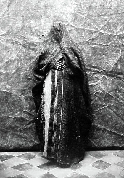 Tunisia, Sfax: studio installation, a veiled Arab woman looking with an eye in traditional clothing and jewellery, 1902
