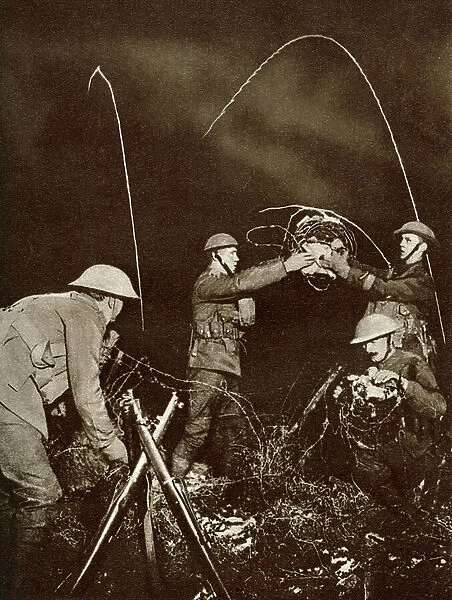 A wiring party. Soldiers erecting barbed wire entanglements in No Man's Land under cover of darkness during World War One. From The Story of 25 Eventful Years in Pictures published 1935