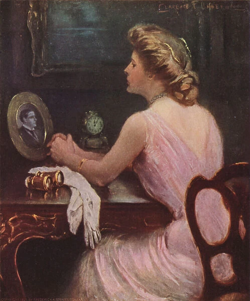 Woman sitting at her dressing table looking at a photograph of a man, possibly her husband or lover (colour litho)