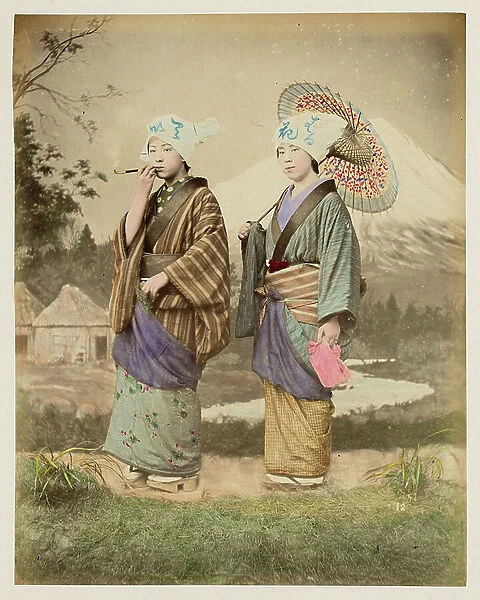 Two young girls travelling (one smokes the pipe, the other wears an umbrella), in front of a painted decor from Mount Fuji - Japanese travellers - Japan 1880-1910 - Hand coloured photo