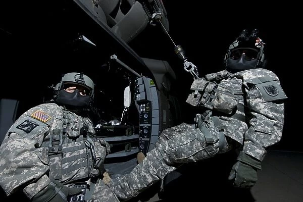Crew Chief sits in the doorway of a UH-60 Black Hawk while medic sits on the hoist