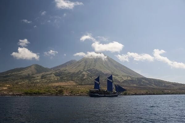 An Indonesian pinisi schooner sails near a remote volcanic island