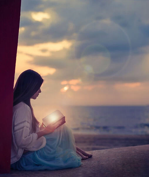 Woman sitting on a beach with illuminated book