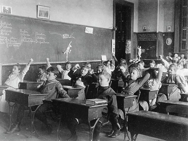 Children seated at desks in Washington, D.C. classroom, stretching, (1899?). Creator: Frances Benjamin Johnston