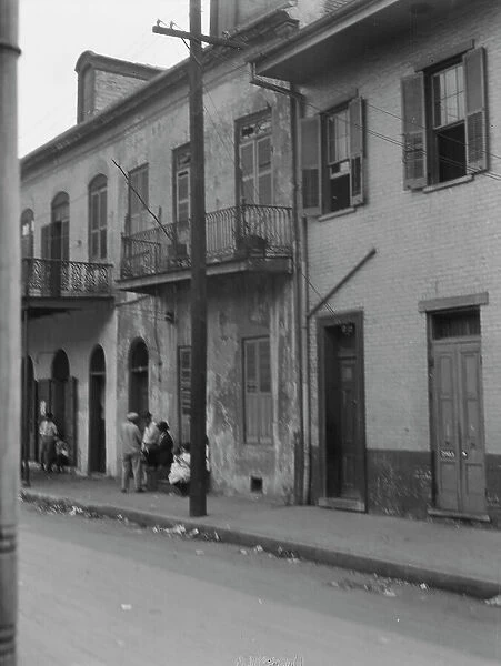 View from across street of four people talking in the French Quarter, New Orleans, c1920-1926. Creator: Arnold Genthe