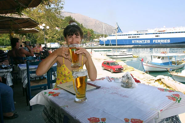 Woman enjoying a drink in a harbourside taverna, Poros, Kefalonia, Greece