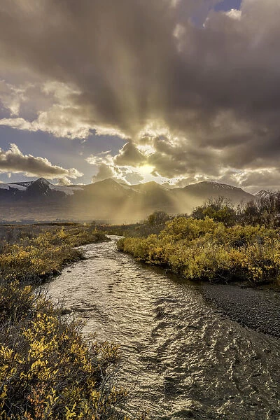 Coast Mountain Range with rays of sunlight beaming across a stream and autumn tundra, Alaska, USA