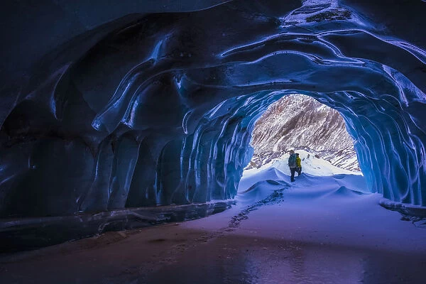 A Hiker Exits A Small Ice Cave While Exploring The Terminal Moraine Of Black Rapids Glacier In The Winter; Alaska, United States Of America