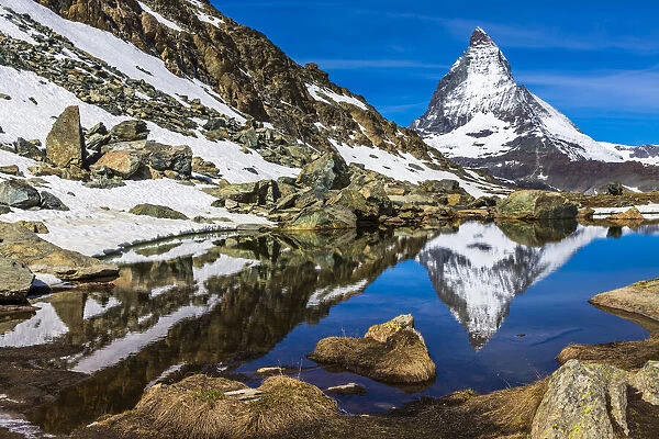 Large rocks and scree from surrounding mountains with the Matterhorn reflected in a small lake near Riffelsee, Zermatt, Switzerland