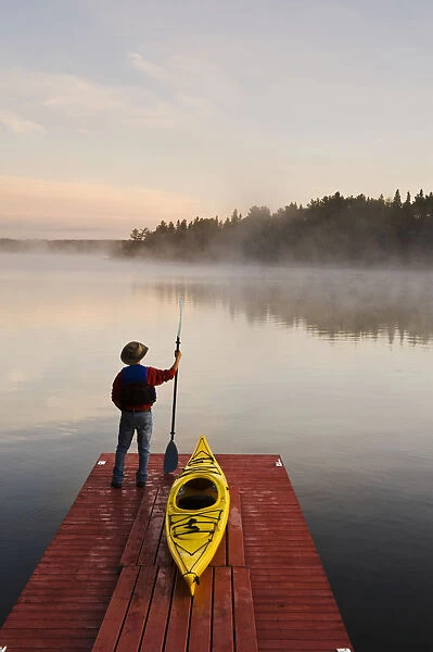 Man Standing By Kayak On Dock In Northwestern Ontario; Lake Of The Woods Ontario Canada