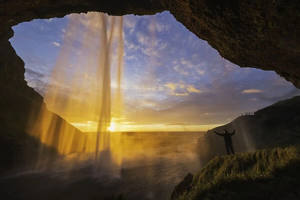 Man Standing Behind The Waterfall Known As Seljandafoss Along The Southern Coast Of Iceland; Iceland