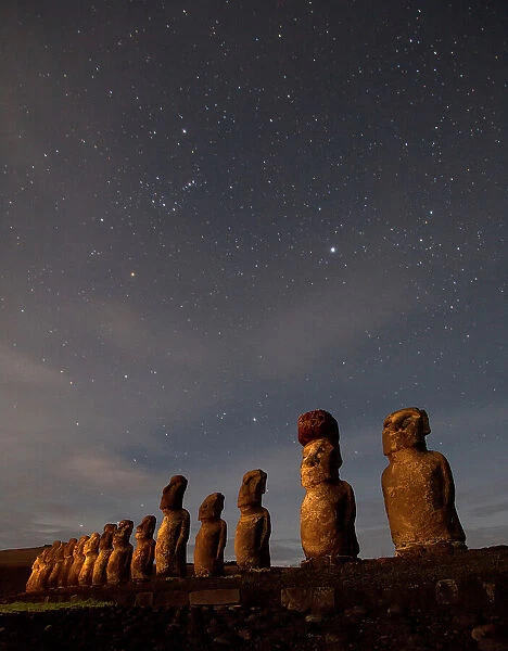 Moai stand at night illuminated beneath a sky full of stars
