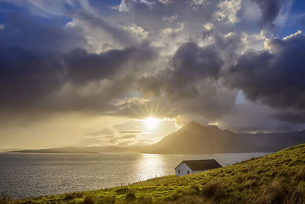 Rooftop of a house along the Scottish coast with sun shining through the dramatic clouds over Loch Scavaig on the Isle of Skye in Scotland, United Kingdom