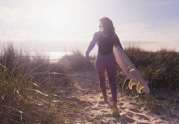 A woman carries her surfboard down a sandy path to the beach; Tarifa cadiz andaulsia spain