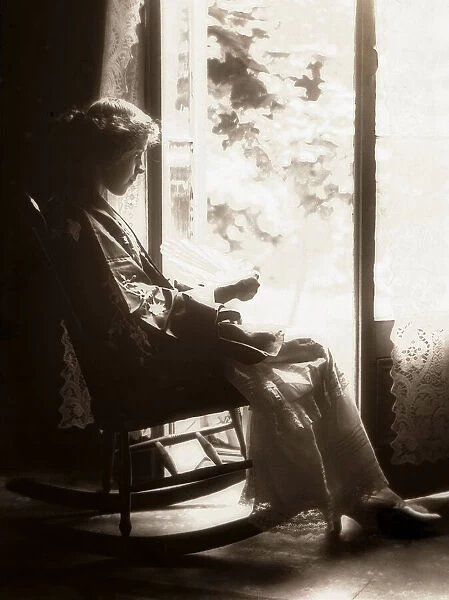 Woman in a rocking chair in front of the window, circa 1900