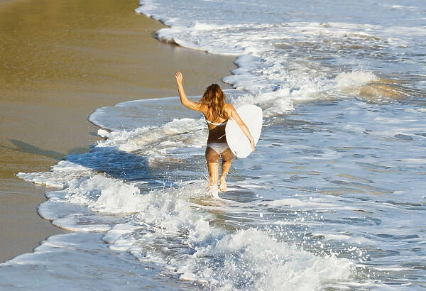 Woman running along beach with surfboard; Tarifa, Cadiz Province, Andalusia, Spain