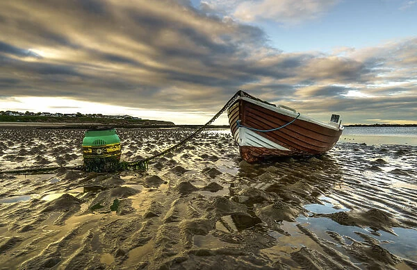 A Wooden Boat Tied To The Shore Sitting On Wet Sand At The Waters Edge At Sunset; Whitburn, Tyne And Wear, England