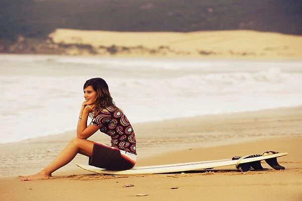 Young Woman Sitting On Her Surf Board On The Beach; Tarifa, Cadiz, Andalusia, Spain