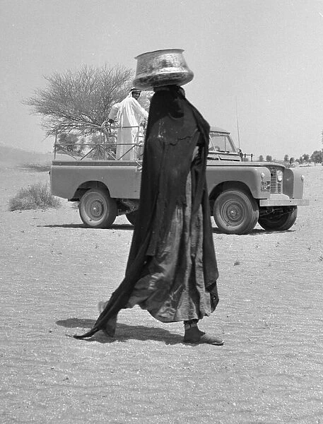A bedouin woman seen here wearing traditional dress collecting water. July 1965