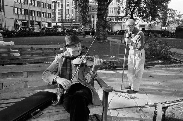 Stephan Grappelli playing his violin in Hanover Square, London watched by park sweeper