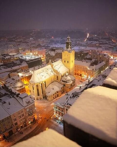 Gorgeus cityscape of winter Lviv city with roofs covered by snow from top of town hall, Ukraine, Europe. Latin Cathedral glowing by city lights