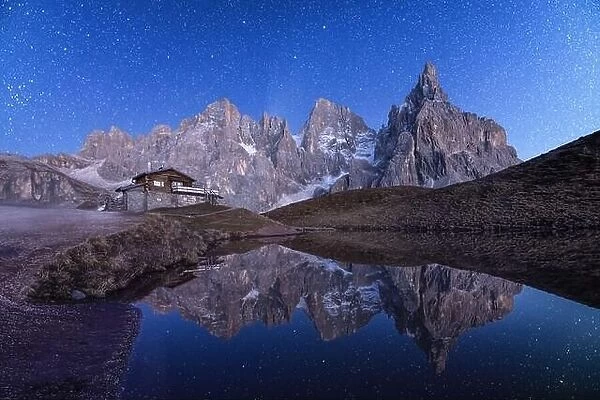 Incredible night landscape with a reflection of starry sky and mountains in a water of small lake in a popular tourist destination - Baita Segantini