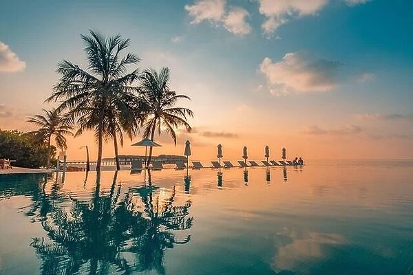 Luxury poolside on the beach with sunset colors. Amazing luxury summer background. Idyllic sunset beach scene, infinity pool in luxury resort, tropic