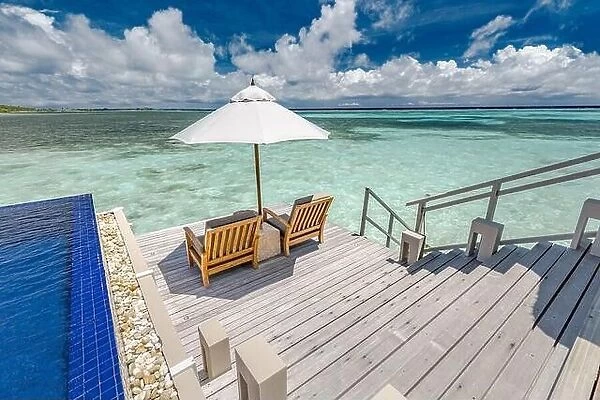 Luxury swimming pool in over water villa with beach chairs and umbrella. Amazing summer vibes, sea view and luxurious couple scene. Tropical paradise