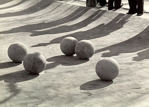 balls arranged on the ground. Their shadows are mixed with those of the men standing on the margins of the court